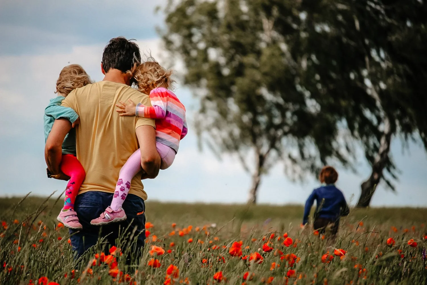 Vater trägt zwei Kinder über eine Blumenwiese