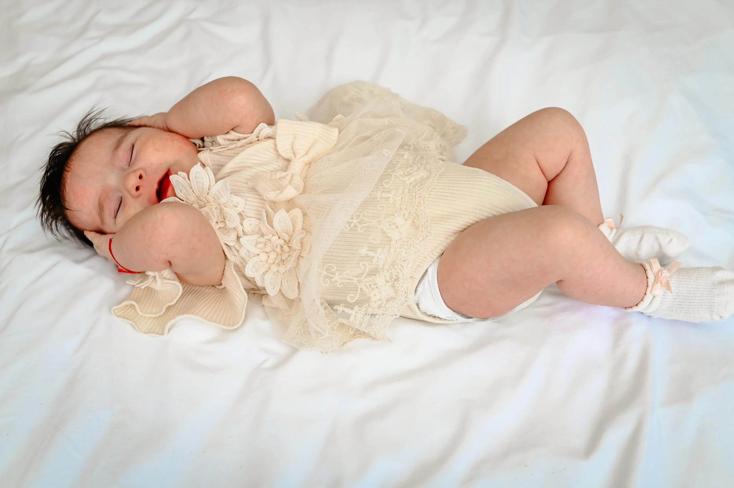 Baby in einem hellen Outfit auf einer weißen Decke